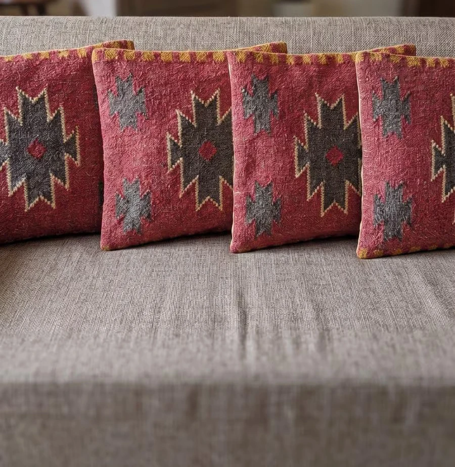 A set of red woven cushion covers with charcoal, slate and gold-edged geometric motifs on a neutral sofa.